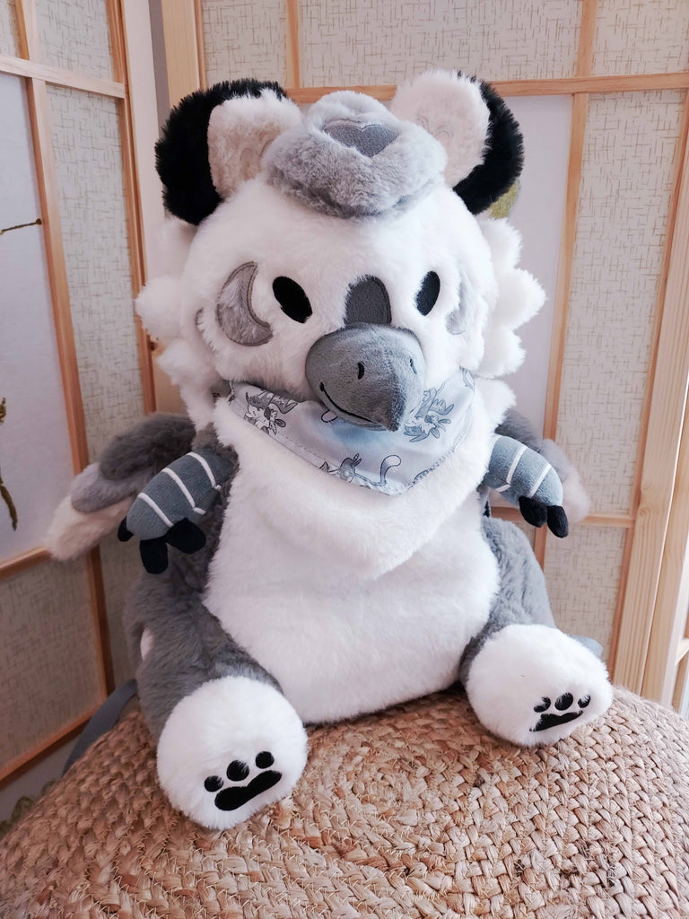 Plush backpack of Sesame the grey and white gryphon, wearing a light grey bandana