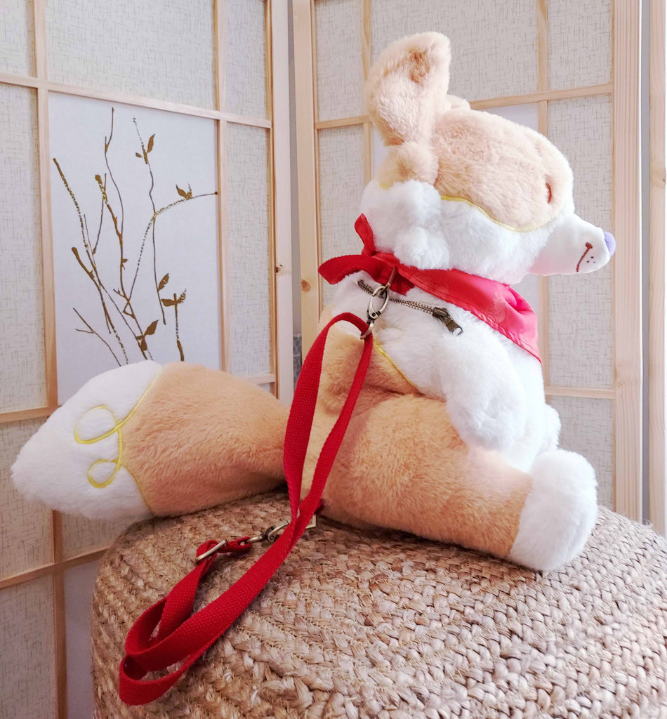 Side view of a plush backpack of Sunny Pup the red border collie wearing a red bandana, with red backpack straps