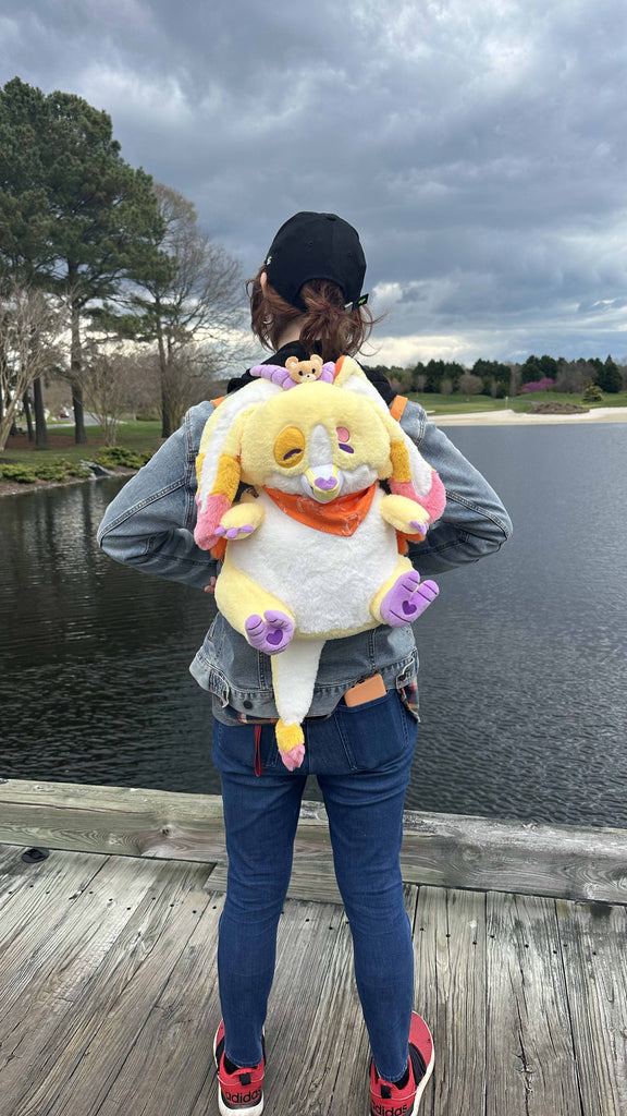 Person wearing a plush backpack of Charmy the yellow dragon while standing on a bridge looking out at the water