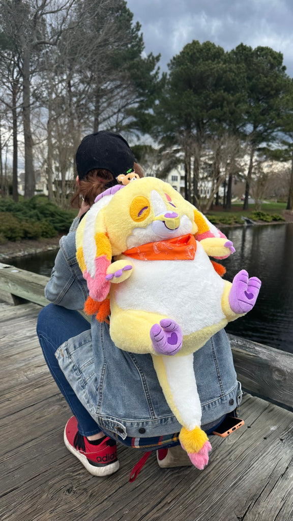 Person wearing a plush backpack of Charmy the yellow dragon while standing on a bridge overlooking water