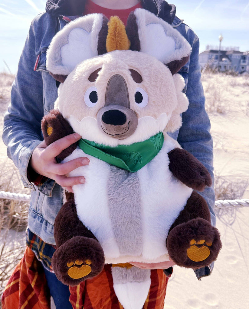 Person holding a plush backpack of ChocoChip the Hyena while at the beach