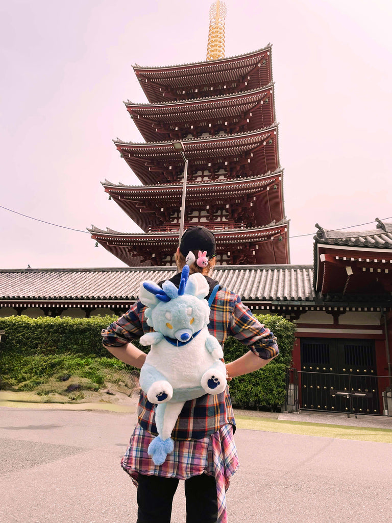 Person wearing a plush backpack of Cloud the blue dragon while standing by a building in Japan