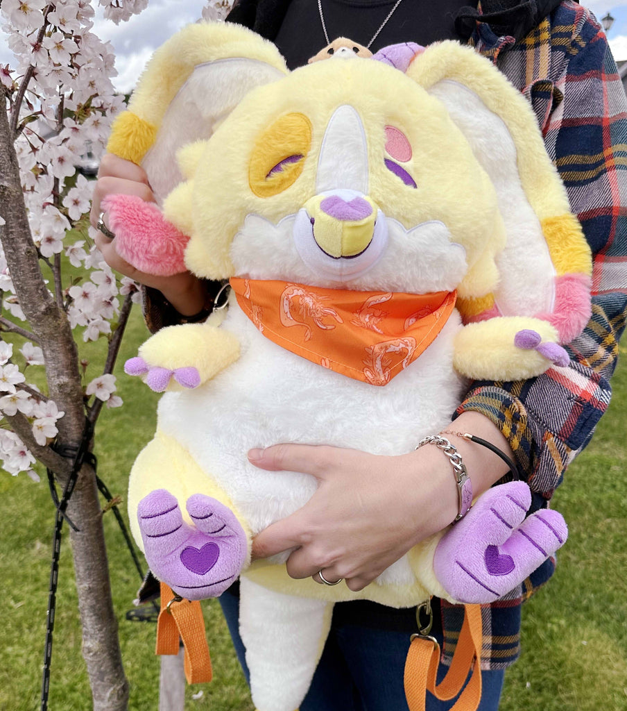 Person holding a plush backpack of Charmy the yellow dragon while standing next to a flowering tree