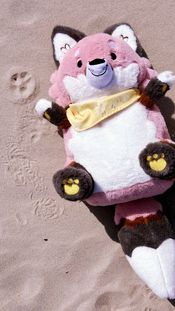 Plush backpack of Chiffon the fox lying in the sand at the beach, next to a paw print