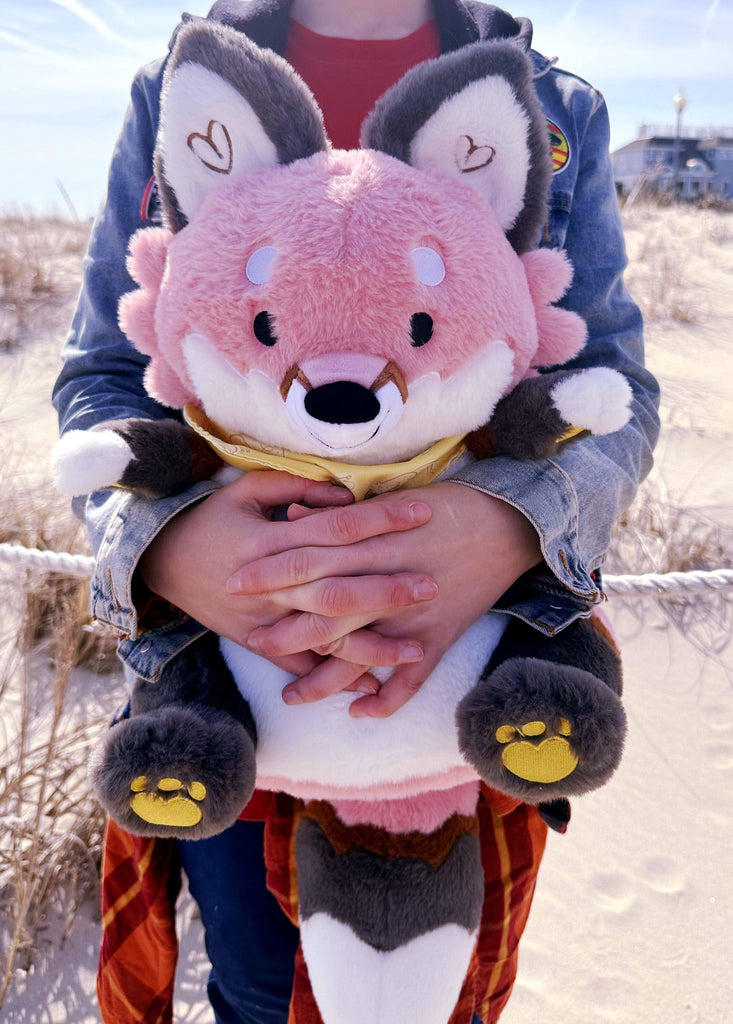 Person holding a plush backpack of Chiffon the fox while at the beach