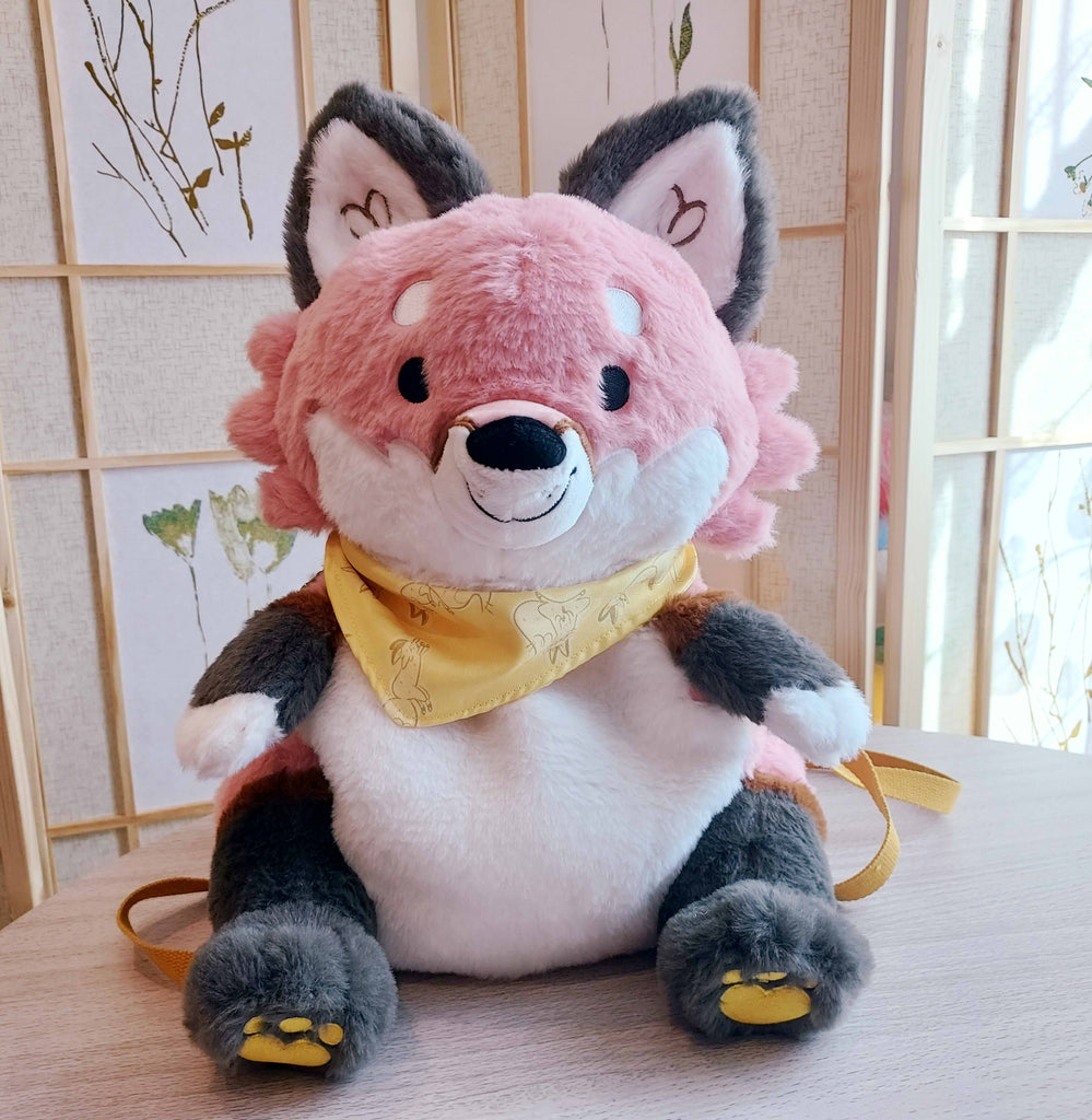 Plush backpack of Chiffon the fox wearing a yellow bandana, with yellow backpack straps
