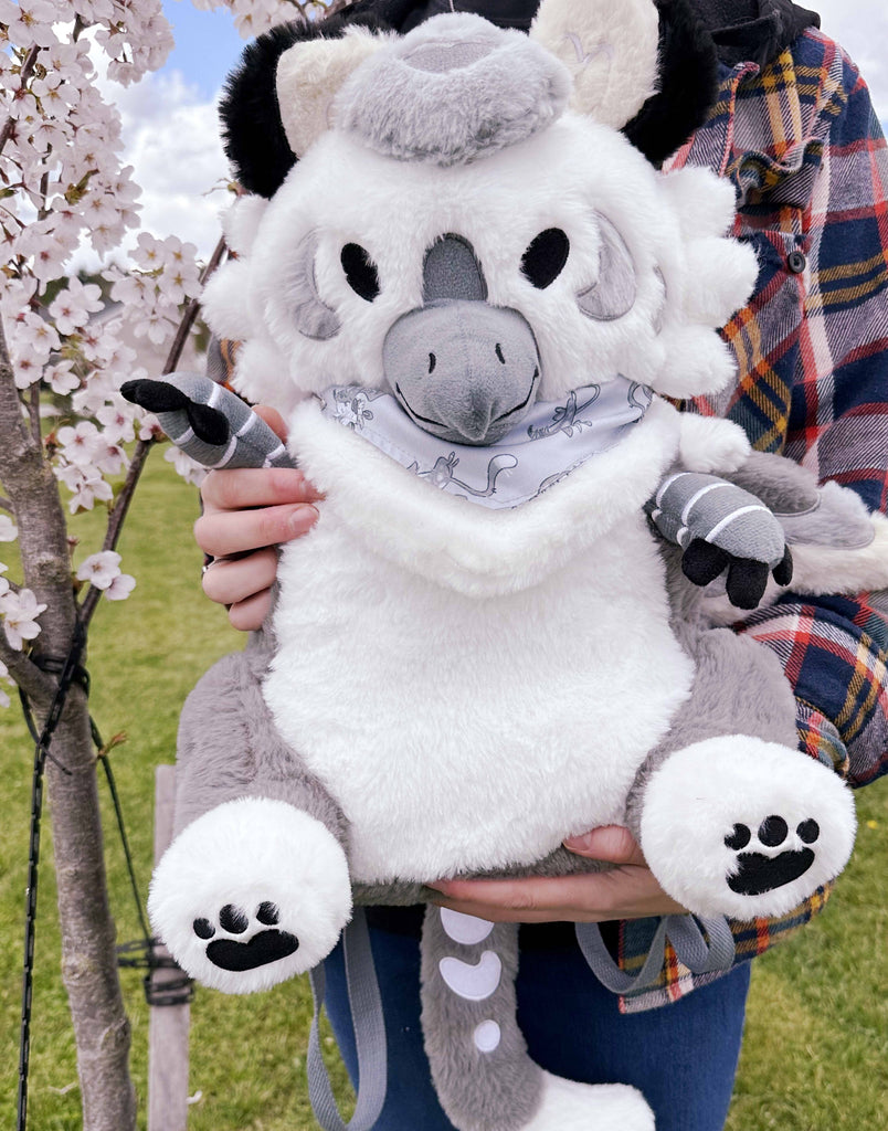 Person holding plush backpack of Sesame the grey and white gryphon