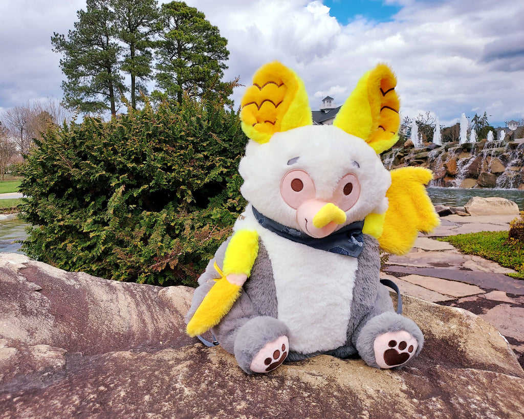 Plush backpack of lemon the bat sitting outside by a waterfall