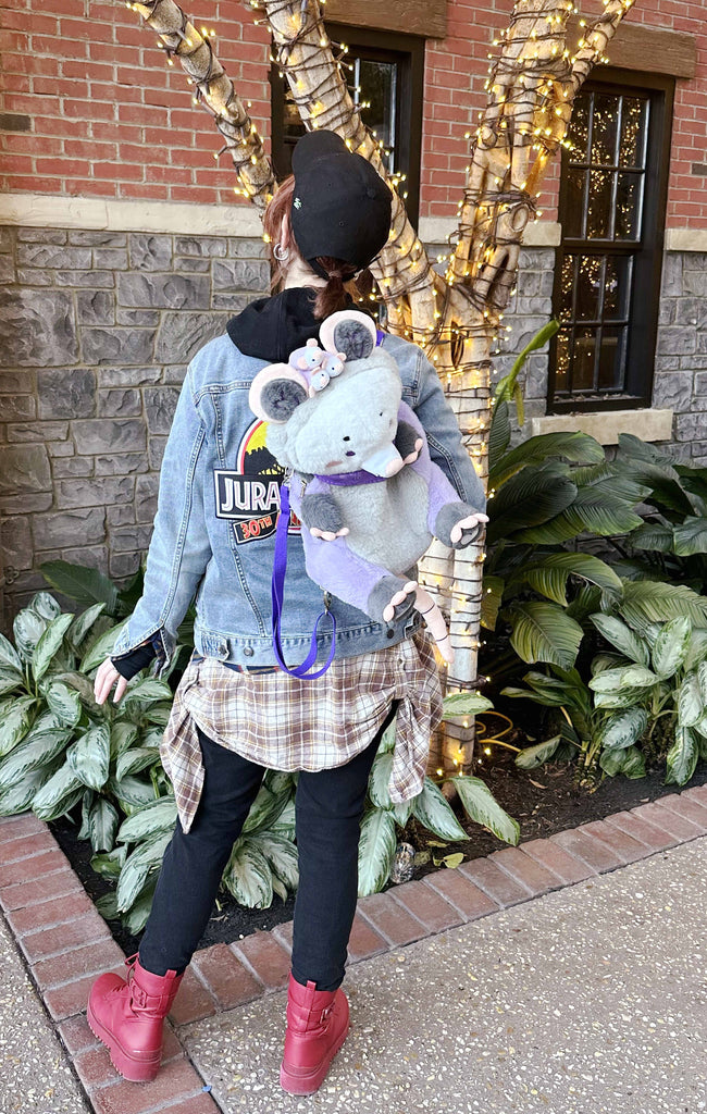 Person wearing a plush backpack of Plum the possum while standing by a tree