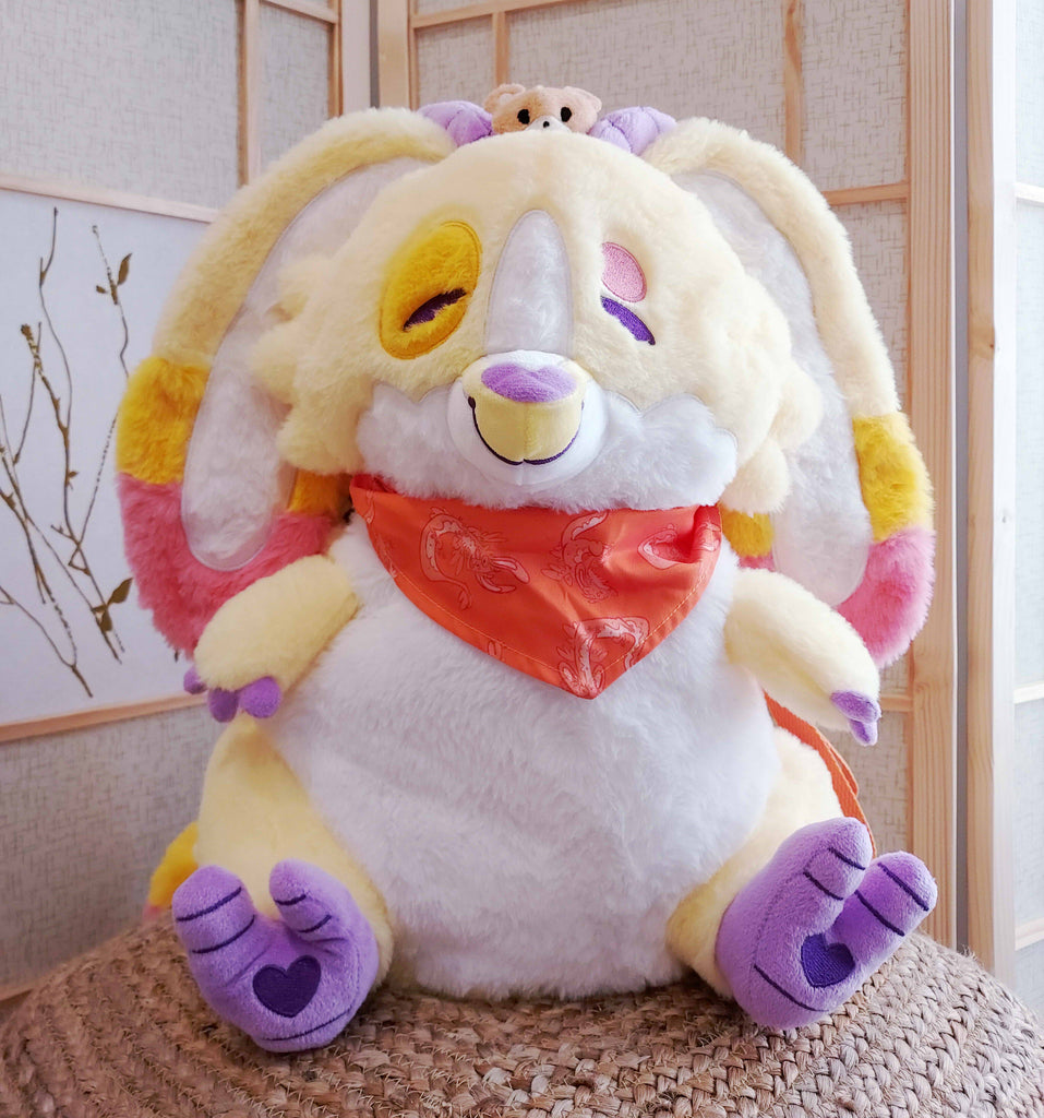 Plush backpack of Charmy the yellow dragon wearing an orange bandana, with orange backpack straps, and a bear plushie on his head