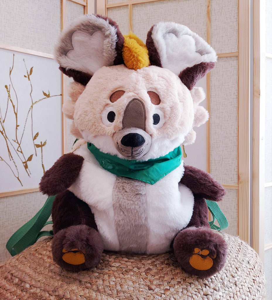 Plush backpack of Chocochip the hyena wearing a green bandana, with green backpack straps
