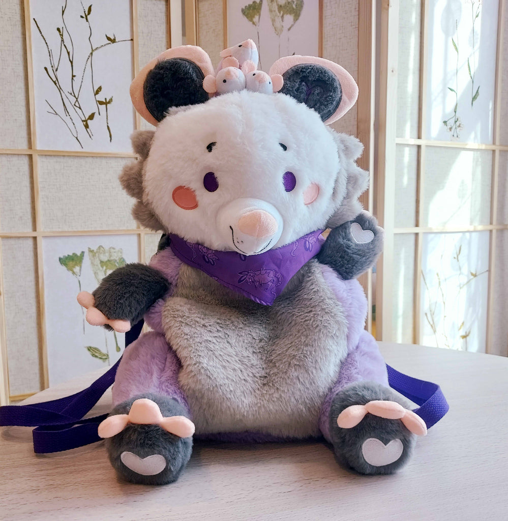 Front view of a plush backpack of Plum the possum wearing a purple bandana, with purple backpack straps
