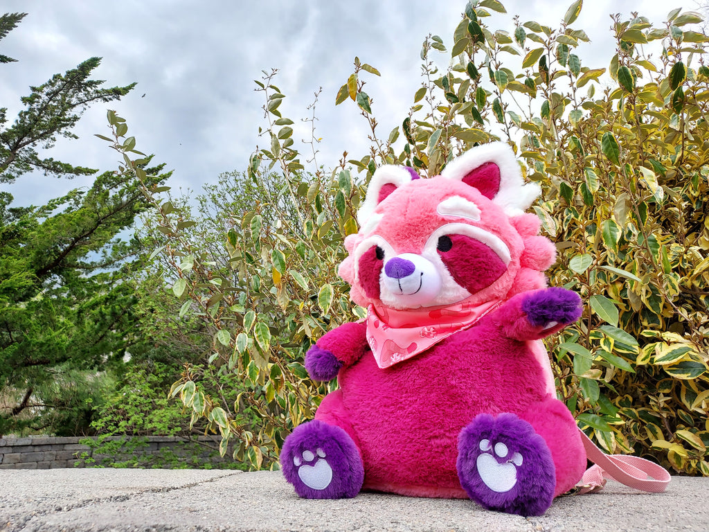 Plush backpack of Raspberry the red panda sitting in a garden 