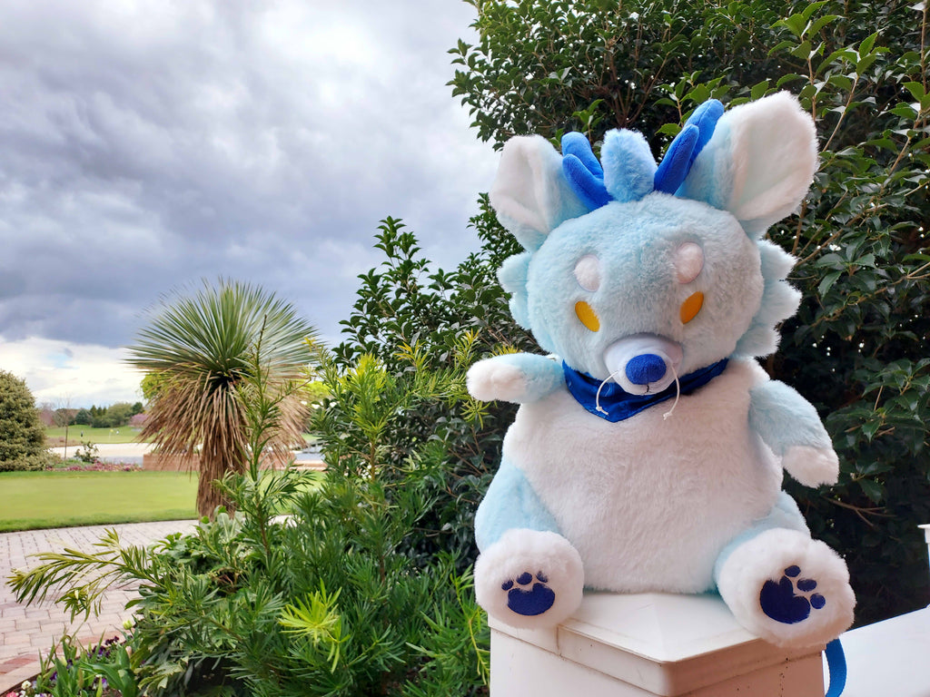 Plush backpack of Cloud the blue dragon sitting on a railing overlooking some trees