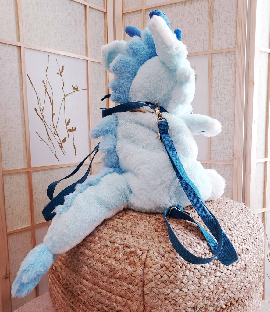 Back view of a plush backpack of Cloud the blue dragon wearing a blue bandana, with blue backpack straps
