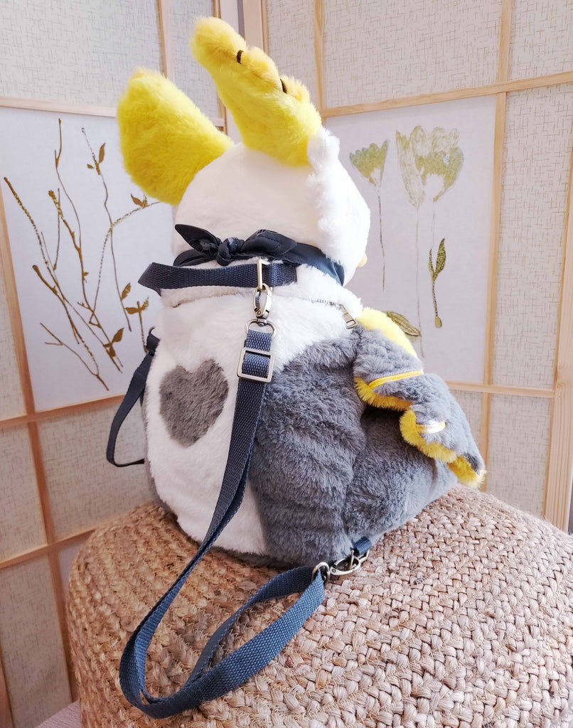 Back view of a plush backpack of Lemon the bat wearing a black bandana, with black backpack straps
