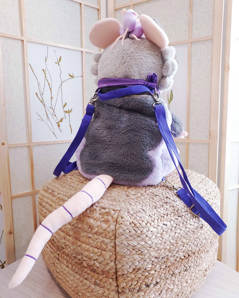 Back view of a plush backpack of Plum the possum wearing a purple bandana, with purple backpack straps