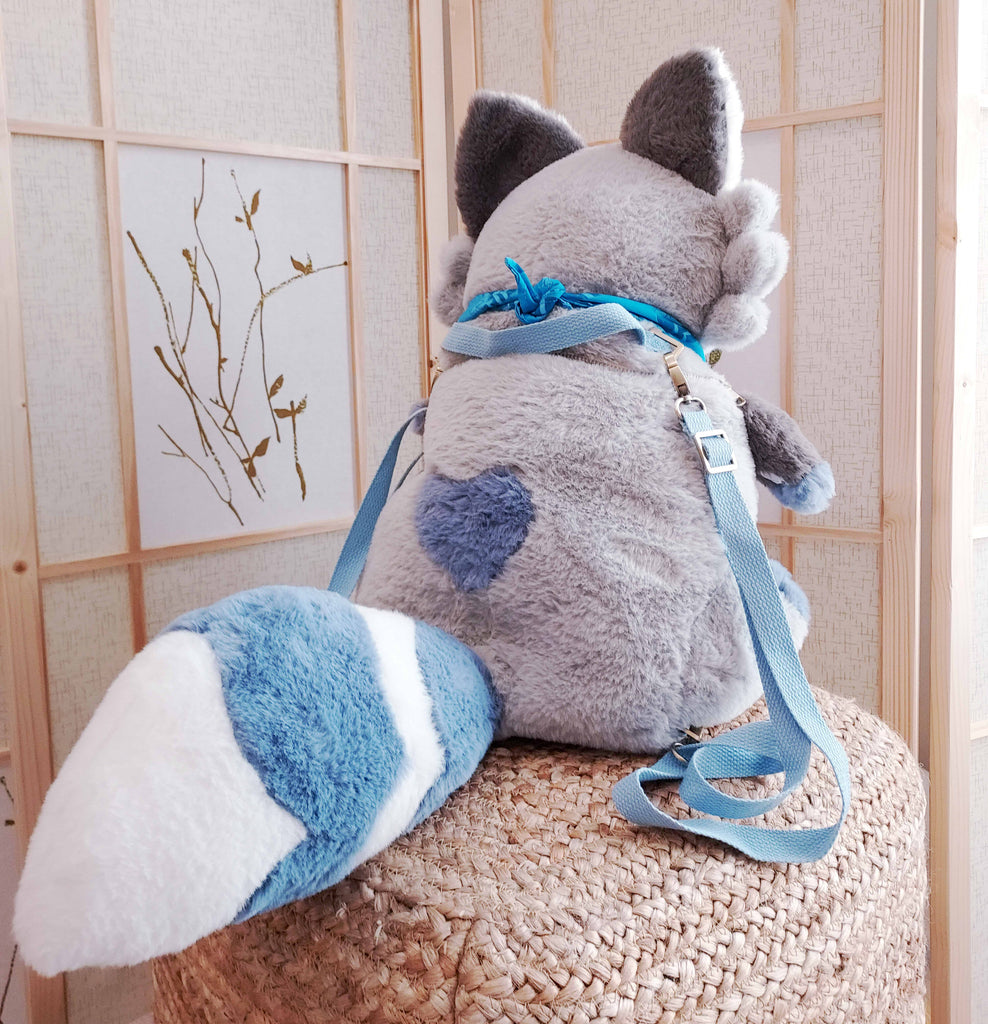 Back view of a plush backpack of Peanut the raccoon wearing a blue bandana, with blue backpack straps