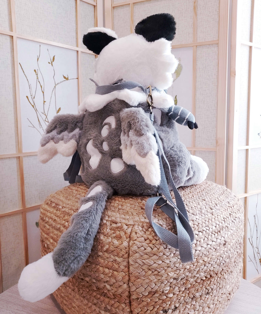 Back view of a plush backpack of Sesame the grey and white gryphon, who has light grey backpack straps