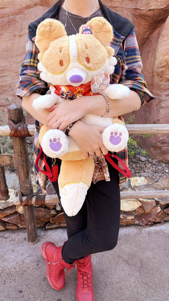 Person holding a plush backpack of Sunny Pup the red border collie wearing a red bandana, with red backpack straps