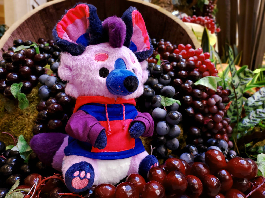 Berry the purple, blue, and pink Hyena sitting in a basket of grapes