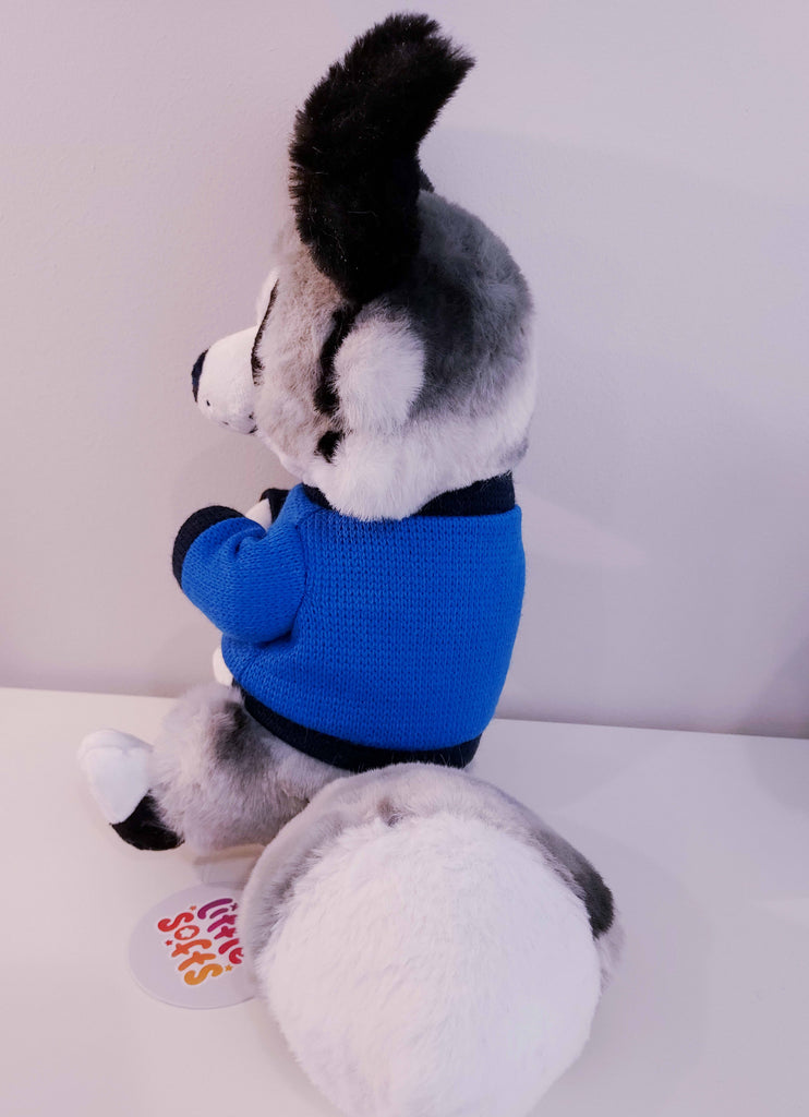 Side view of a plush toy of a blue merle border collie wearing a blue and black sweater