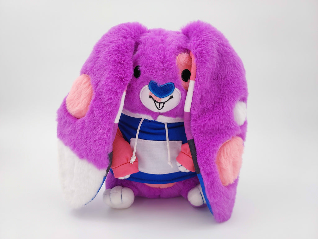 Plush toy of Bubblegum the purple, pink, black,white, and blue bunny wearing a colorful hoodie, with their ears covering their face