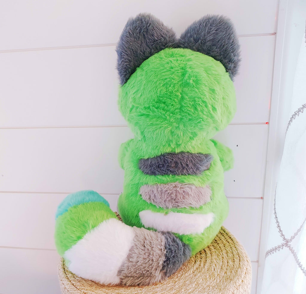 Back view of a plush toy of Matcha the cat who is green, black, white, and grey, wearing a hoodie