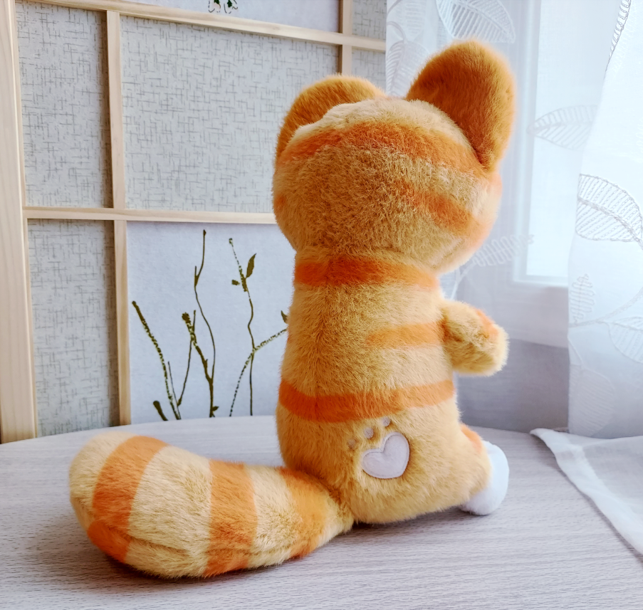 Back view of plush toy of Cheese the orange cat plush with a heart shaped paw print marking in his fur