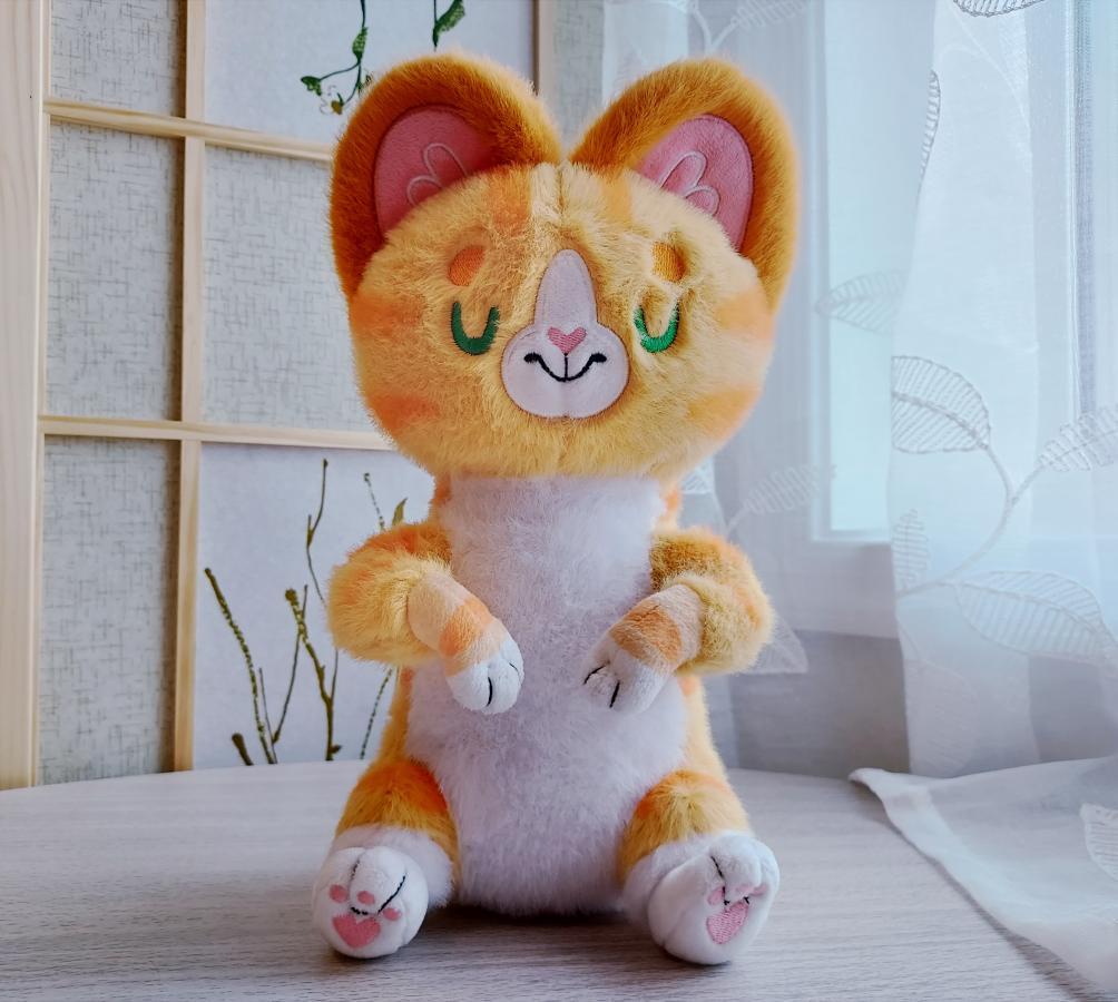 Plush toy of Cheese the orange cat with green embroidered sleeping eyes
