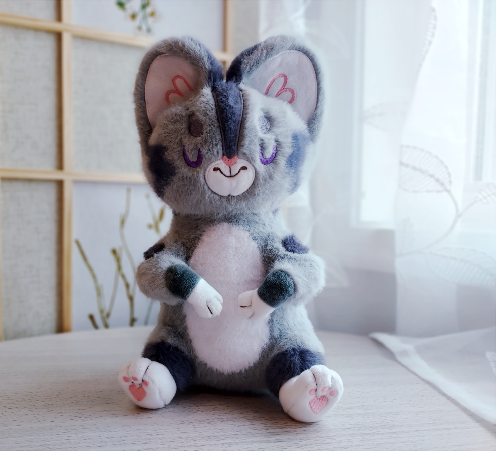 Plush toy of Domino the grey tabby cat with purple embroidered sleeping eyes