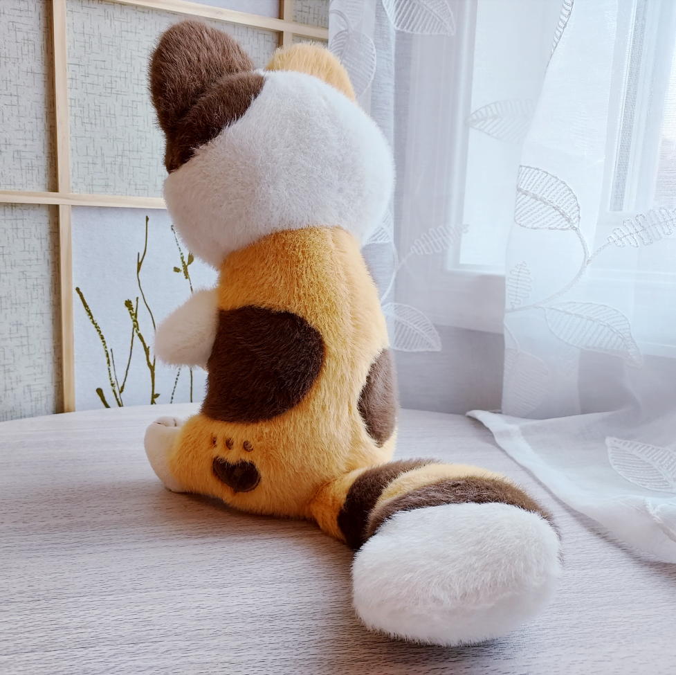 Back view of plush toy of Doodle the calico cat plush with a heart shaped paw print marking in his fur
