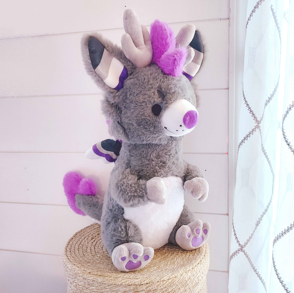 Plush toy of Marshmallow the dragon who is black, white, purple, and grey