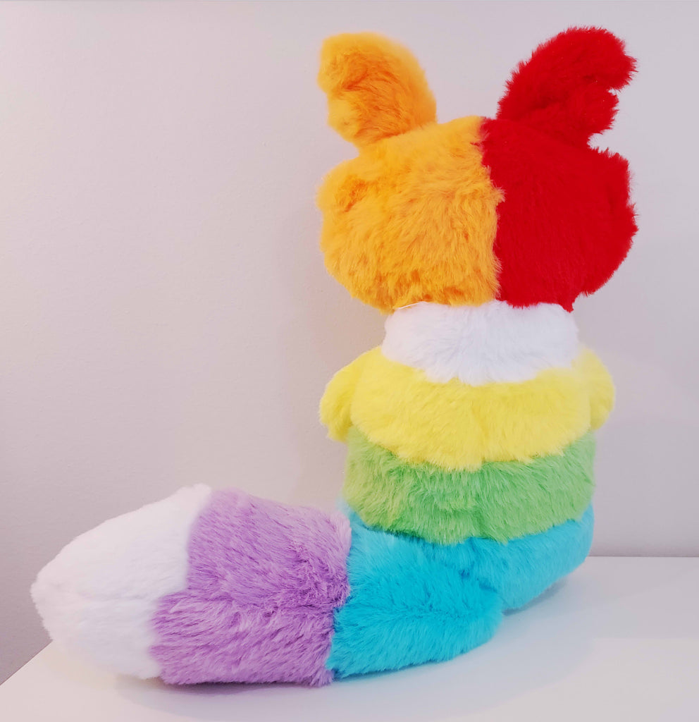 Back view of a plush toy of a rainbow border collie