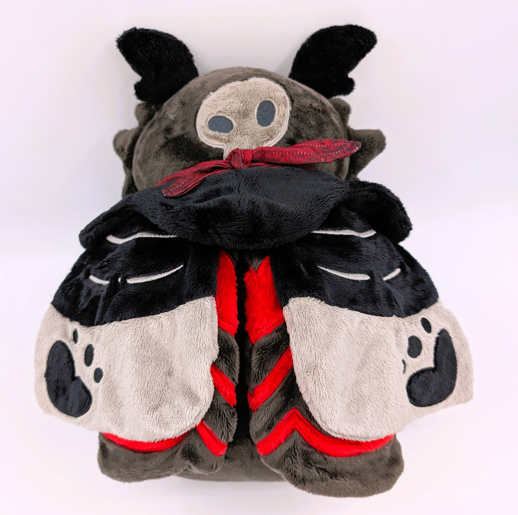 Back of a plush toy of a black and red moth. His wings have grey, red, and white details