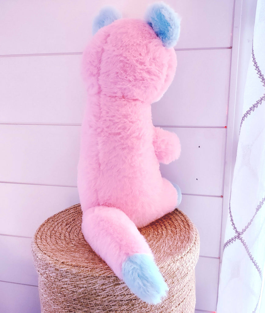 Back view of a plush toy of Cake Pop the otter who is pink, white, and blue 