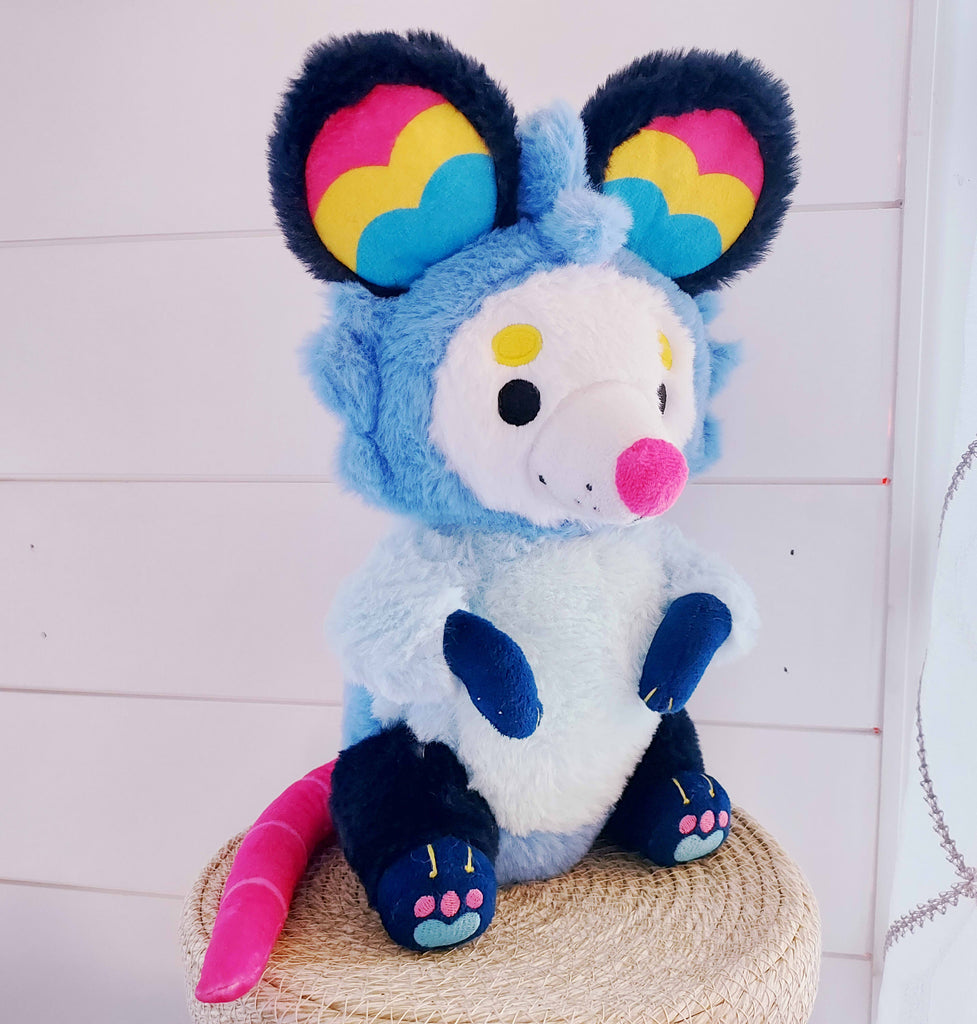 Plush toy of Pancake the possum who is blue, pink, and yellow