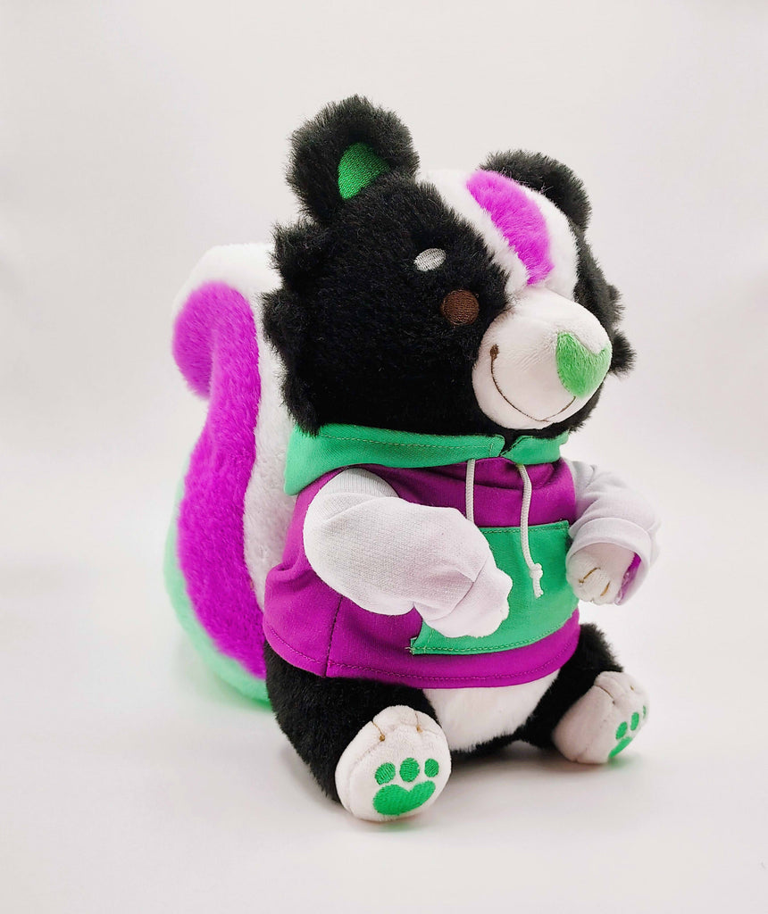 Plush toy of Pepper the green, purple, and white skunk, wearing a matching hoodie