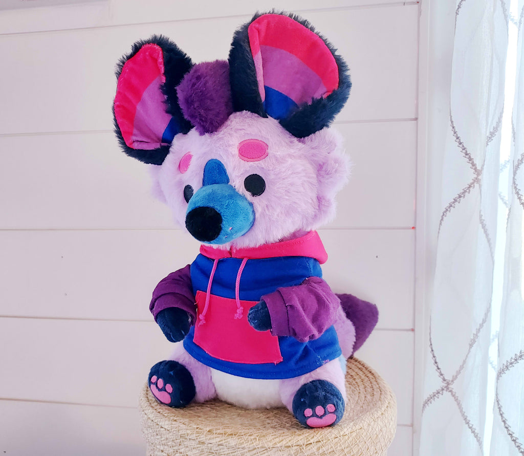 Plush toy of Berry the purple, pink, and blue hyena wearing a hoodie 