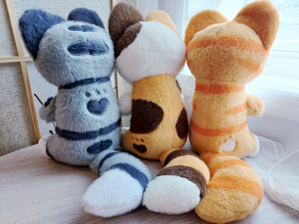 Back view of Snuggle Paws plush of Domino the grey Tabby, Doodle the calico cat, and Cheese the orange cat