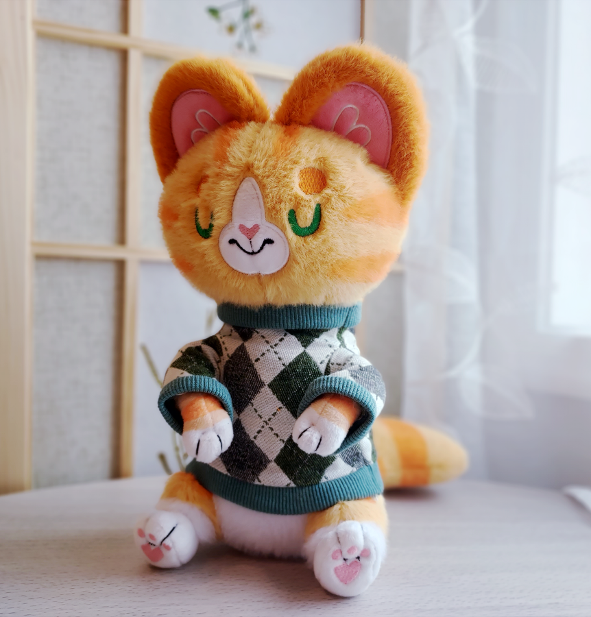 Plush toy of Cheese the orange cat wearing a green argyle sweater
