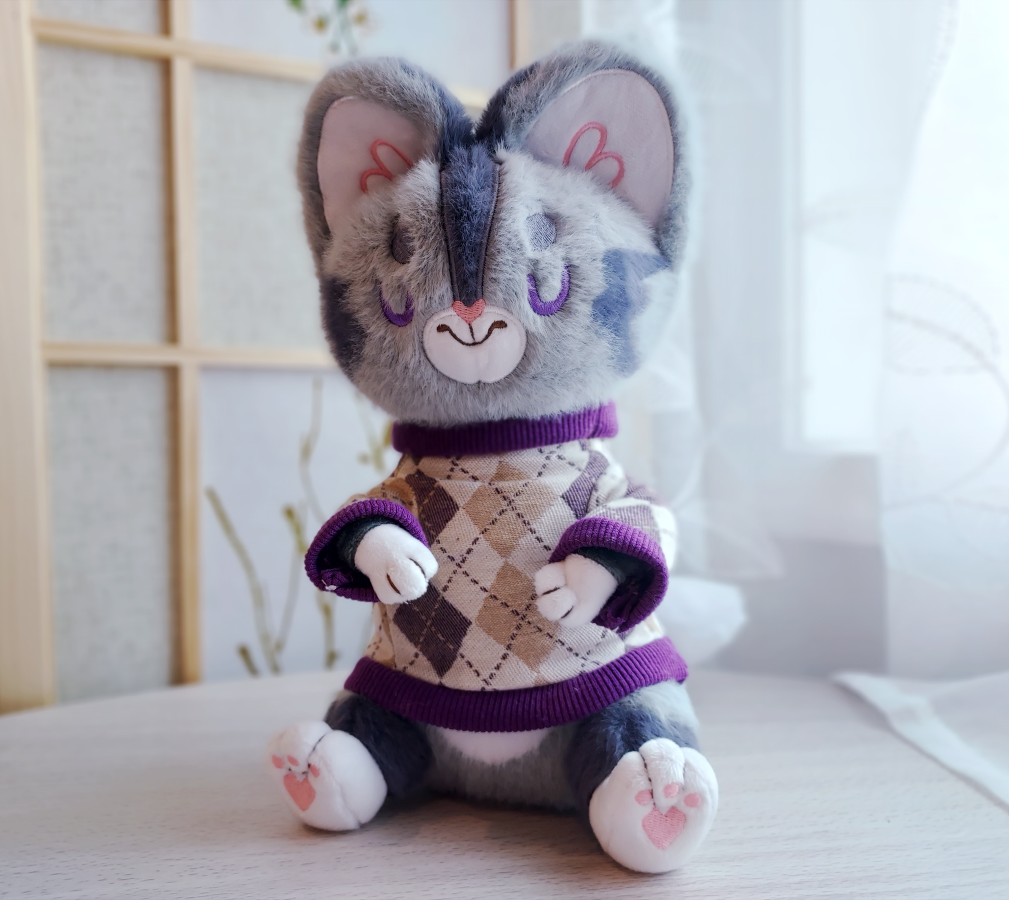 Plush toy of Domino the grey tabby cat wearing a purple argyle sweater