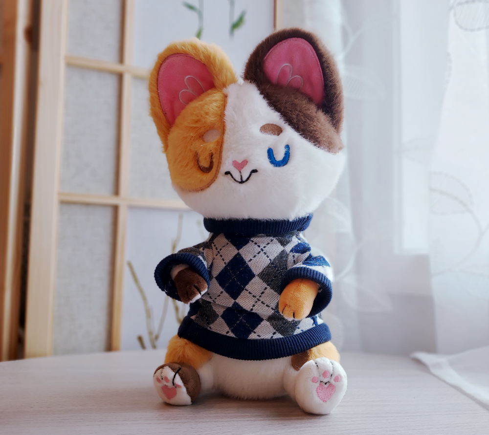 Plush toy of Doodle the calico cat wearing a blue argyle sweater