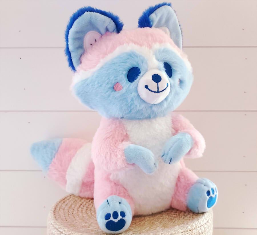 Plush toy of Egg the trans raccoon who is pink, blue, and white 