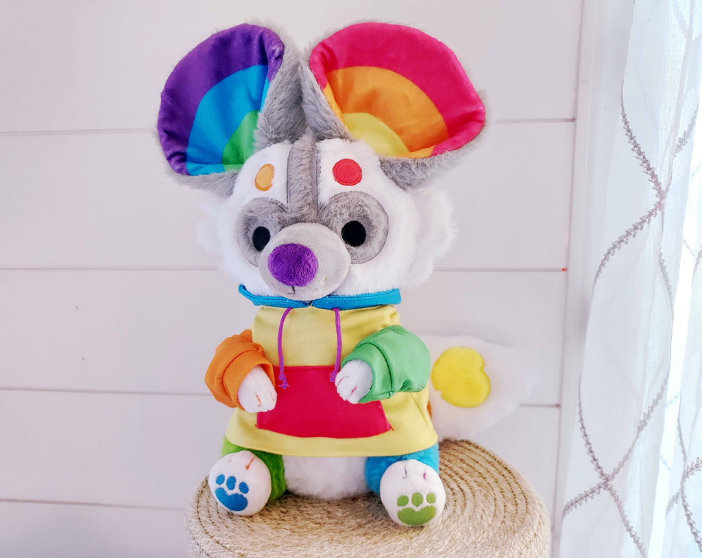 Plush toy of Sprinkles the rainbow painted dog wearing a rainbow hoodie