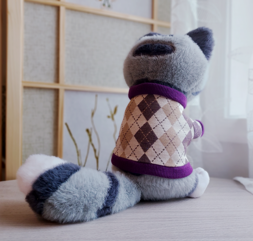 Back view of a plush toy of Domino the grey tabby cat wearing a purple argyle sweater