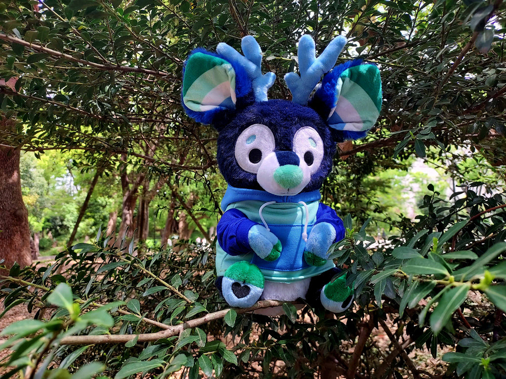 Plush toy of Smoothie the blue and green stag sitting in the forest 