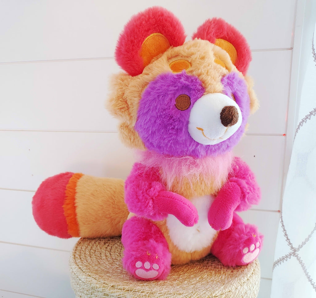 Plush toy of Sweet Potato the tanuki who is pink, purple, red, orange, ad white 