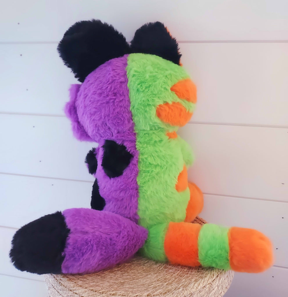 Back view. Snuggle Paws plush of THEM the monstrous abomination. They are half green and orange cat and half purple and black puppy. They have two tails.