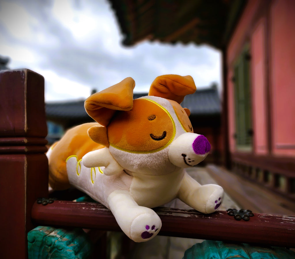 Plush toy of an orange border collie laying on a railing